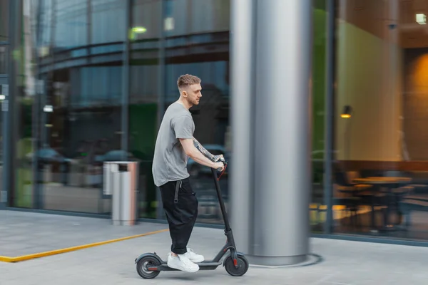 Homem atraente montando uma scooter pontapé no fundo cityscape . — Fotografia de Stock