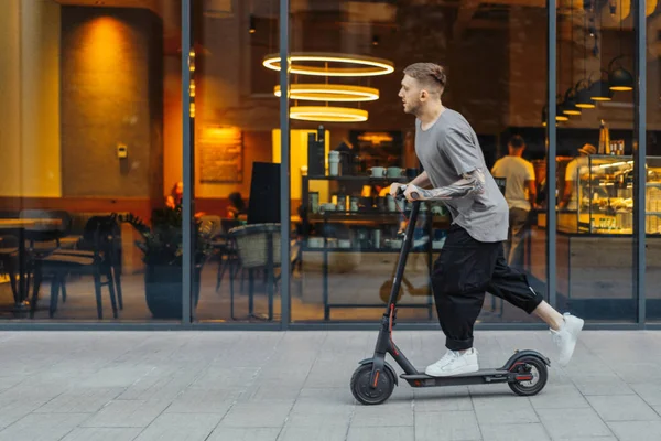 Homem atraente montando uma scooter pontapé no fundo cityscape . — Fotografia de Stock