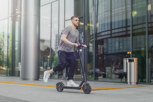 Homem atraente montando uma scooter pontapé no fundo cityscape . — Fotografia de Stock