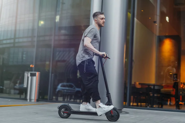 Homem atraente montando uma scooter pontapé no fundo cityscape . — Fotografia de Stock