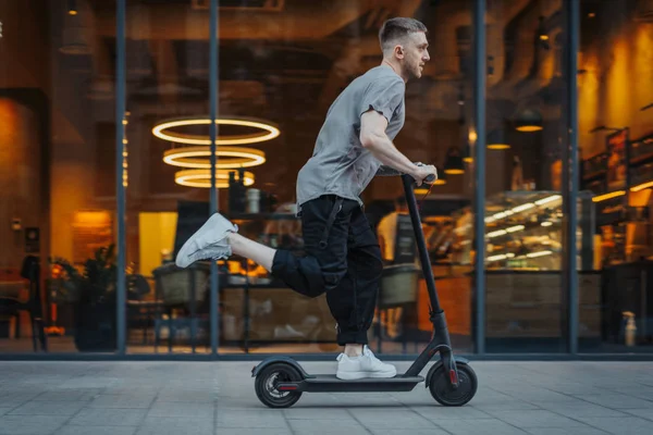 Uomo attraente cavalcando un calcio scooter a sfondo paesaggio urbano . — Foto Stock