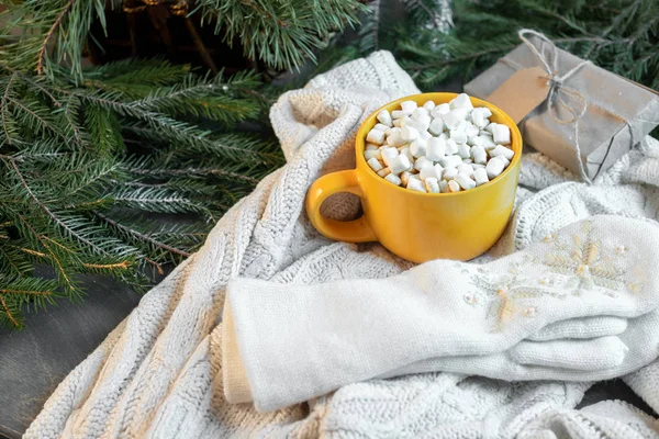 Cup of cacao with Marshmallows and mittens on christmas tree and sweater background.