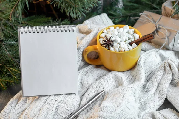 Cup of cacao with Marshmallows and blank notepad on christmas tree and sweater background.