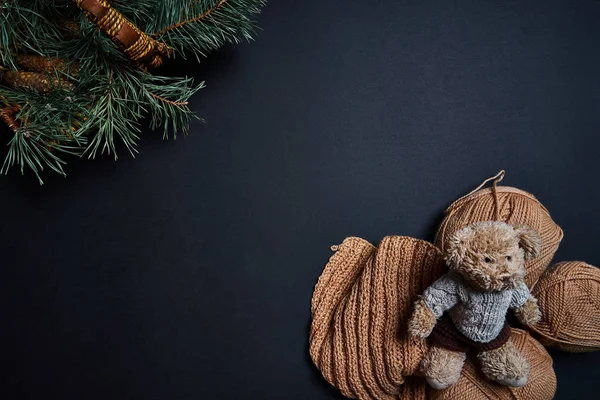 Knitting yarn, bear toy and basket with pine branches on dark background.