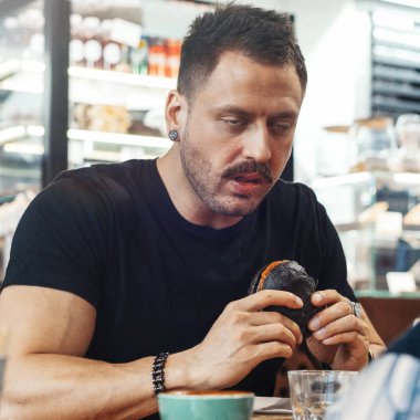 Genç adamın komik surat kafe, taze sulu hamburger yeme yakın çekim.