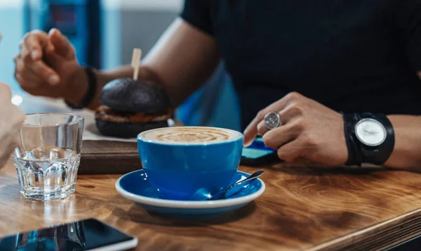 Primer plano de hombre comiendo hamburguesa jugosa fresca negra en la cafetería y beber café . — Foto de Stock