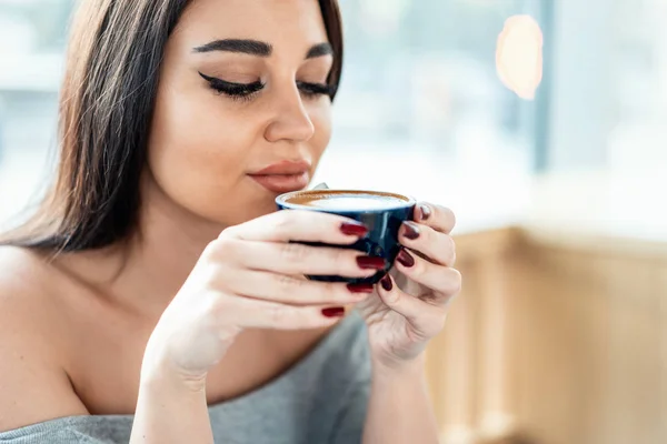 Primer plano de la joven hermosa mujer sosteniendo la taza de café y disfrutando de su aroma . — Foto de Stock