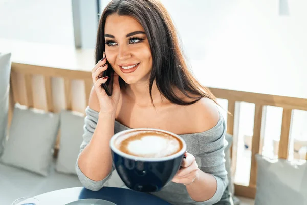 Hermosa mujer sosteniendo enorme taza de café y hablando por teléfono móvil . — Foto de Stock
