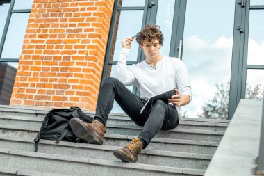 Modern adımlar bina ve Not Defteri'nde yapma oturan dalgın öğrenci.