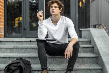 Modern adımlar bina ve Not Defteri'nde yapma oturan dalgın öğrenci.