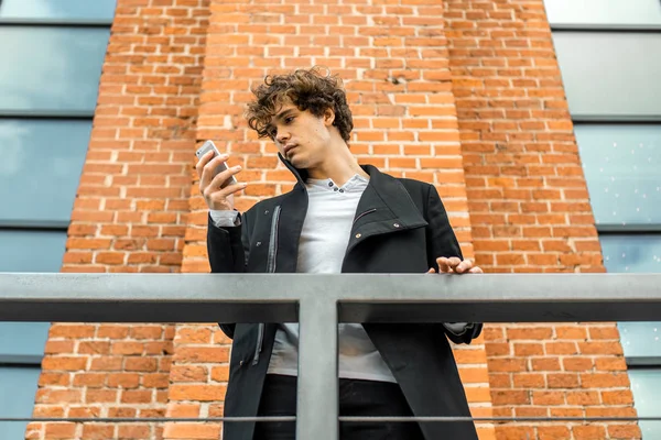 Atraente homem pensativo em pé na escada e olhando para a tela do telefone móvel . — Fotografia de Stock