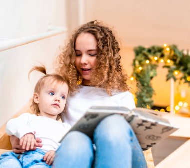 Ablası merdiven, küçük kız kardeşi için yüksek sesle kitap okuma.