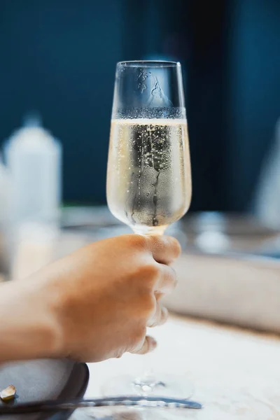 Young woman holding misted glass with champagne in the restaurant. Glass is full with sparkling champagne with bubbles.