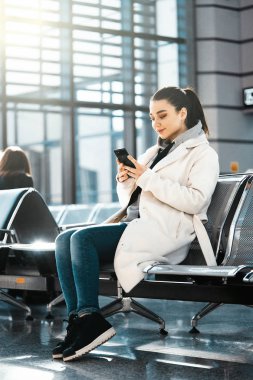 Gülümseyen ve tarafından havaalanında uçuş önce cep telefonu sohbet genç kadın