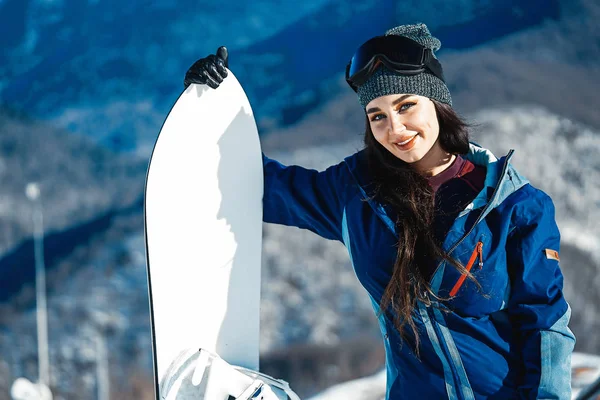 Gülümseyen ve dağ ve yamaç arka plan üzerinde poz snowboard kızın yakın çekim.