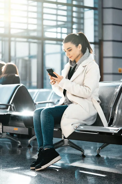 Young woman smiling and chatting by mobile phone in airport before flight — Stock Photo, Image