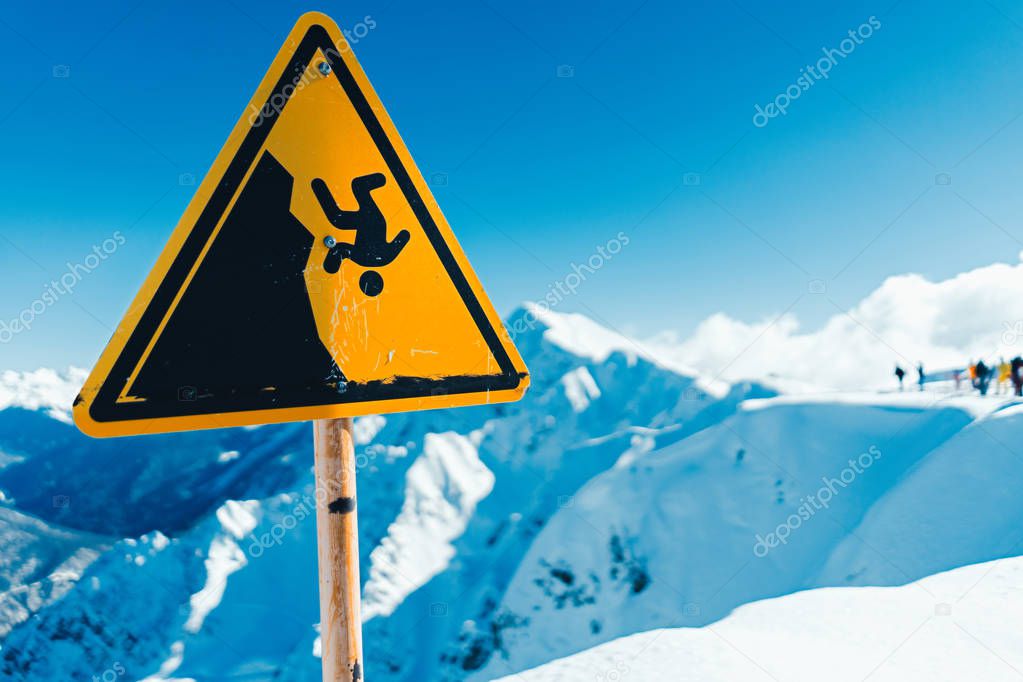 Yellow warning sign in mountain with snowbaorders and ski riders on background.