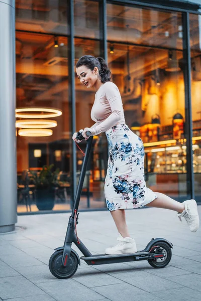 Çağdaş sürme çekici genç kadın tekme scooter cityscape arka plan.