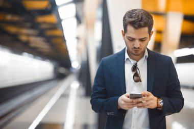 Genç çekici işadamı manifatura mesaj içinde hareket eden telefon için metro tren beklerken. Girişimci sorunları çalışma sürecinde yerleşti. Lating çalışma.
