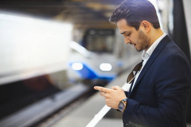 Genç çekici işadamı manifatura mesaj içinde hareket eden telefon için metro tren beklerken. Girişimci çalışma sorunları çözme. Lating çalışma.