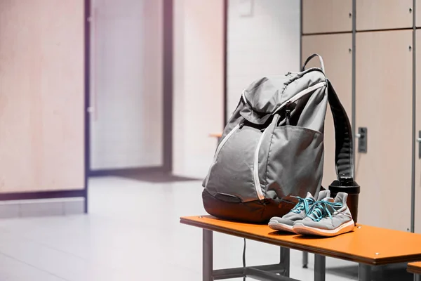 Sports shoes, sport backpack and sport water bottle in gym locker room.