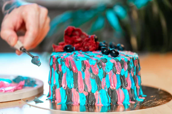 Close up of tattooed man decorating cake with butter colourful cream. — Stock Photo, Image