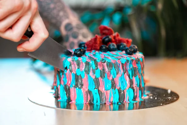 Close up of tattooed man cutting cake with colourful cream.