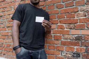 Esmer adam boş kartvizit tuğla arka plan üzerinde gösterilen T-shirt.
