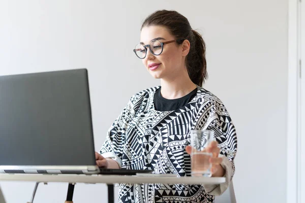 Fiatal, vonzó nő, aki laptopon dolgozik a modern, világos apartmanokban. — Stock Fotó