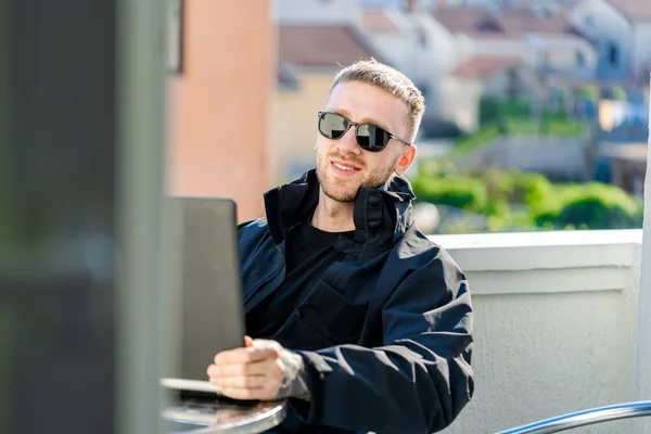 Bonito homem elegante pensativo sentado na varanda e trabalhando no laptop. — Fotografia de Stock