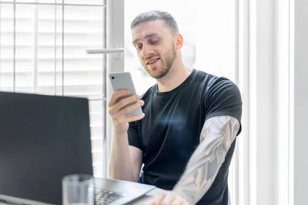 Joven hombre atractivo pensativo trabajando en el ordenador portátil y charlando por teléfono móvil — Foto de Stock