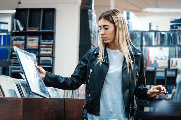 Νεαρή ελκυστική γυναίκα επιλέγει δίσκο βινυλίου σε δισκοπωλείο μουσικής. — Φωτογραφία Αρχείου
