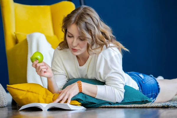 금발의 여자 독서 책 에 홈 과 누워 에 이 바닥 옆 노란색 안락 의자 — 스톡 사진