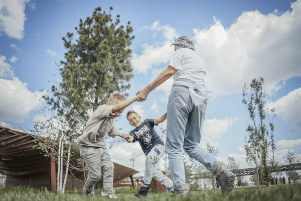 Joven mamá rubia dando la vuelta, girando con sus hijos en el parque . —  Fotos de Stock