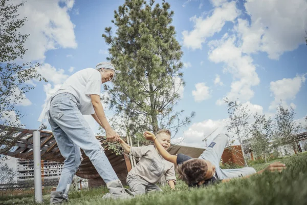 Junge blonde Mutter dreht sich um und wirbelt mit ihren Söhnen im Park. — Stockfoto