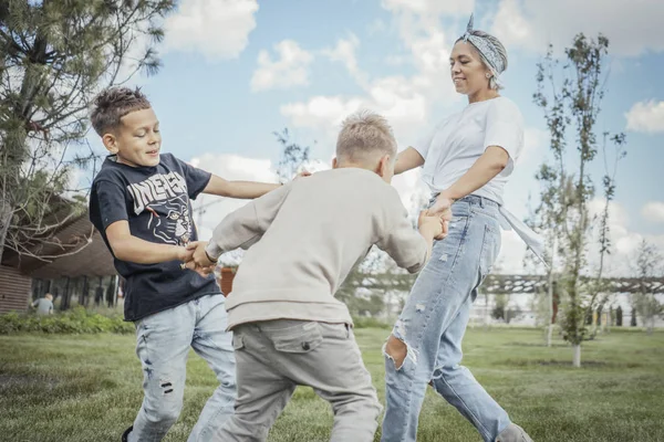 Joven mamá rubia dando la vuelta, girando con sus hijos en el parque . —  Fotos de Stock