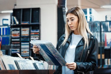 Young attractive woman choosing vinyl record in music record shop. clipart