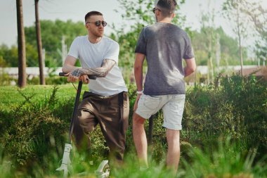 Park manzara elektrikli tekme scooter yanında konuşan iki yakışıklı erkek