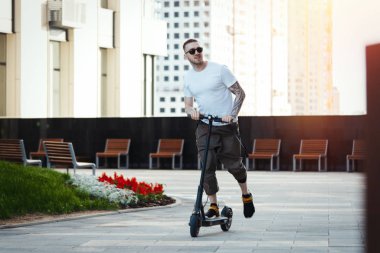 Cityscape arka planda elektrikli kick scooter sürme çekici adam.