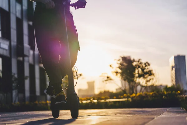 Gros plan de l'homme chevauchant scooter électrique noir coup de pied au paysage urbain au coucher du soleil — Photo