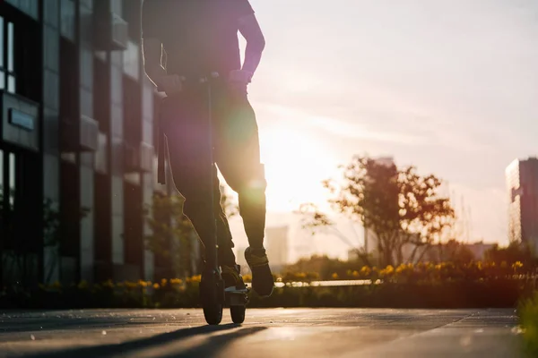 Primer plano del hombre montando scooter eléctrico negro en el paisaje urbano al atardecer —  Fotos de Stock