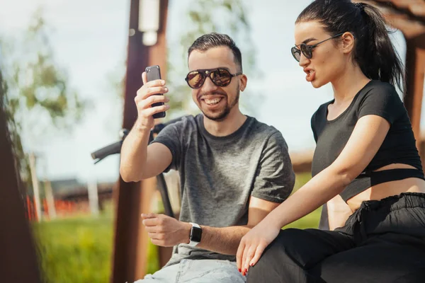 Pareja de hombres y mujeres jóvenes sentados en el parque y haciendo selfies . — Foto de Stock