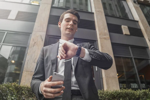 Biznesmen, trzymając telefon w rękę i patrząc na zegarki z bliska. — Zdjęcie stockowe