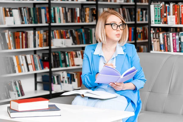 Młoda atrakcyjna kobieta robi kilka notatek w Notatniku w bibliotece. — Zdjęcie stockowe