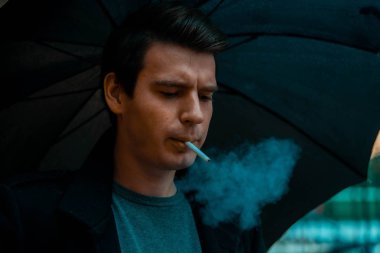 Yağmurlu günde parkta yürüyen şemsiyeli genç dalgın yakışıklı adam.