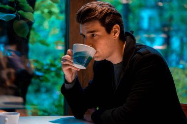 Yakışıklı adam yağmurlu bir günde çay veya kahve içiyor ve pencereden bakıyor.