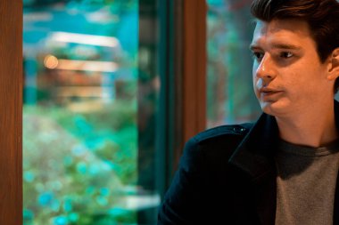 Yakışıklı adam yağmurlu bir günde çay veya kahve içiyor ve pencereden bakıyor.