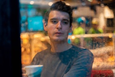 Yakışıklı adam yağmurlu bir günde çay veya kahve içiyor ve pencereden bakıyor.