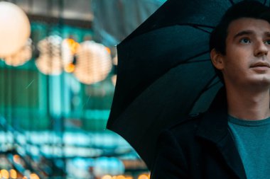 Yağmurlu günde parkta yürüyen şemsiyeli genç dalgın yakışıklı adam.