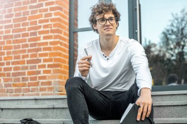 Modern bina ve Not defteri elinde tutan adımlar üzerinde oturan dalgın adam.